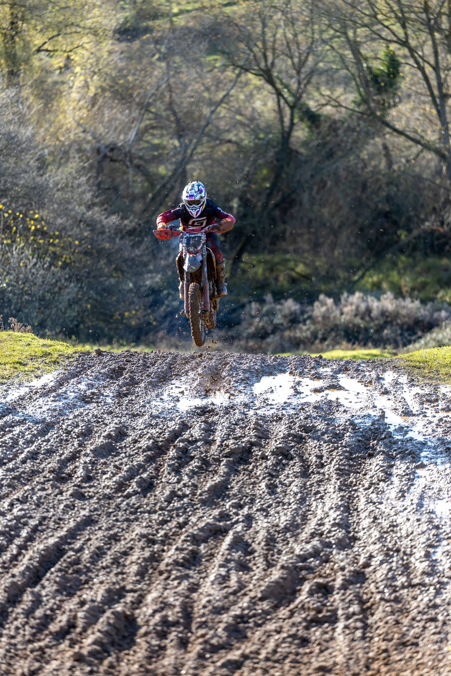 Motocross rider jumping over a muddy dirt track on a red dirt bike, race photographed by LJPhotostop.