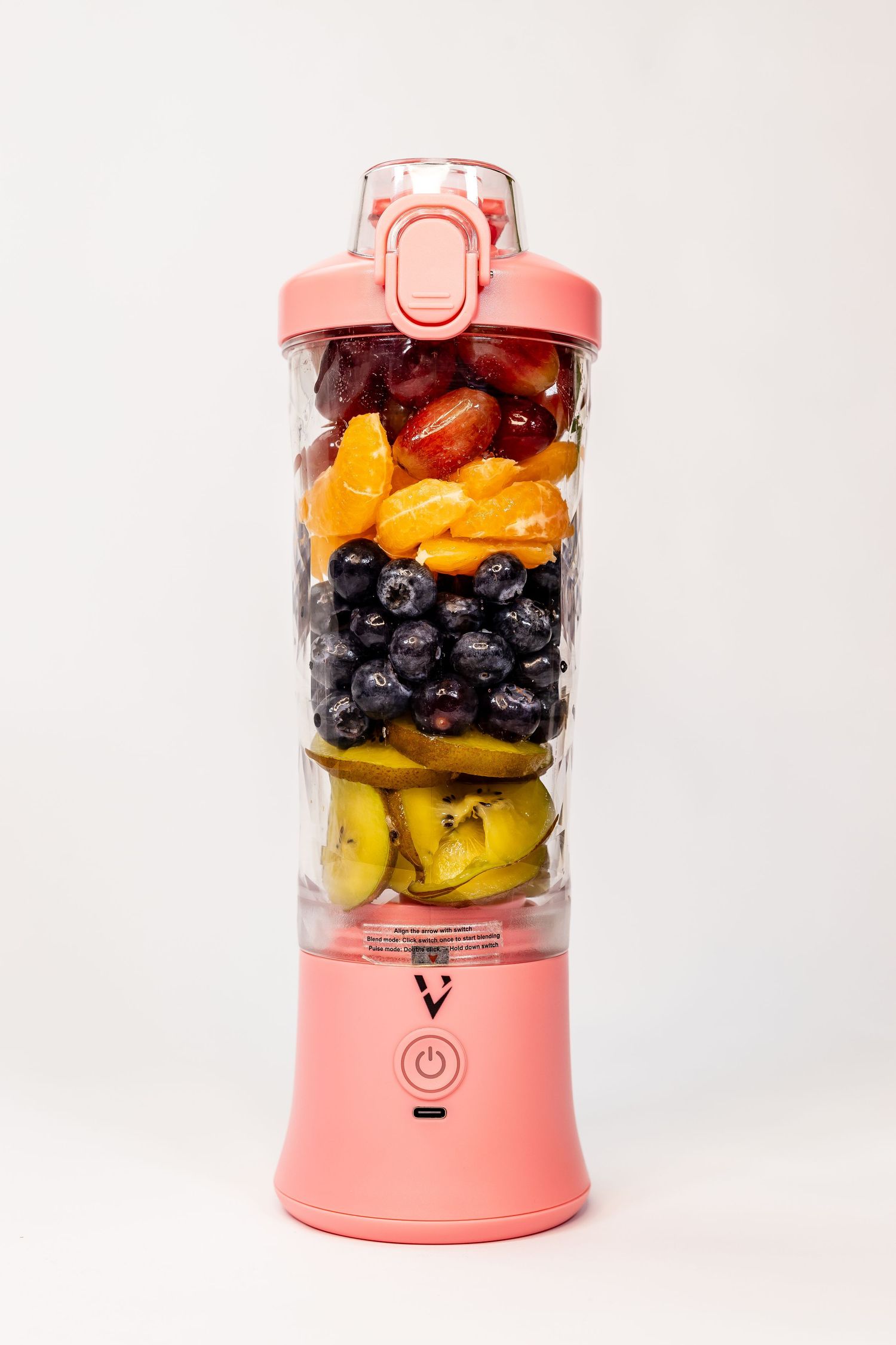 Pink portable personal blender filled with fresh mixed fruits including blueberries and bananas.