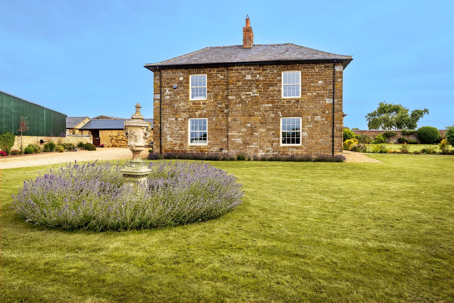 Traditional stone country house with manicured lawn, lavender garden bed, and ornamental urn in foreground.
