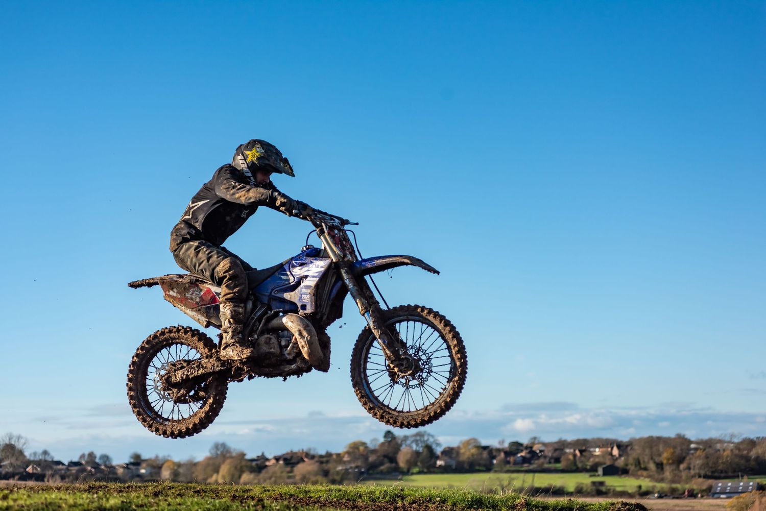 Motocross rider performing a high jump on a dirt bike against a clear blue sky.