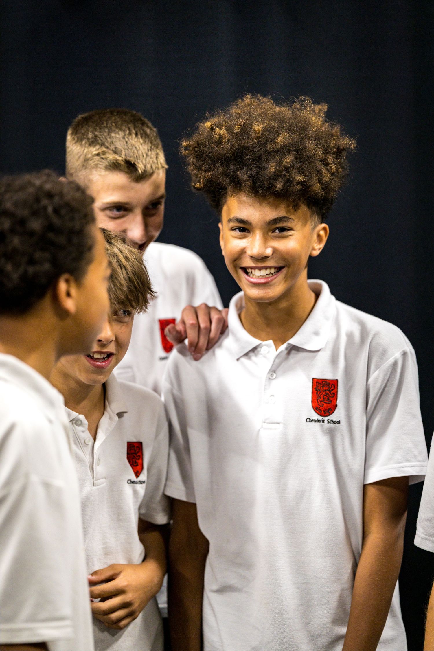 Group of smiling teenage school boys in white polo shirts socializing and laughing together.