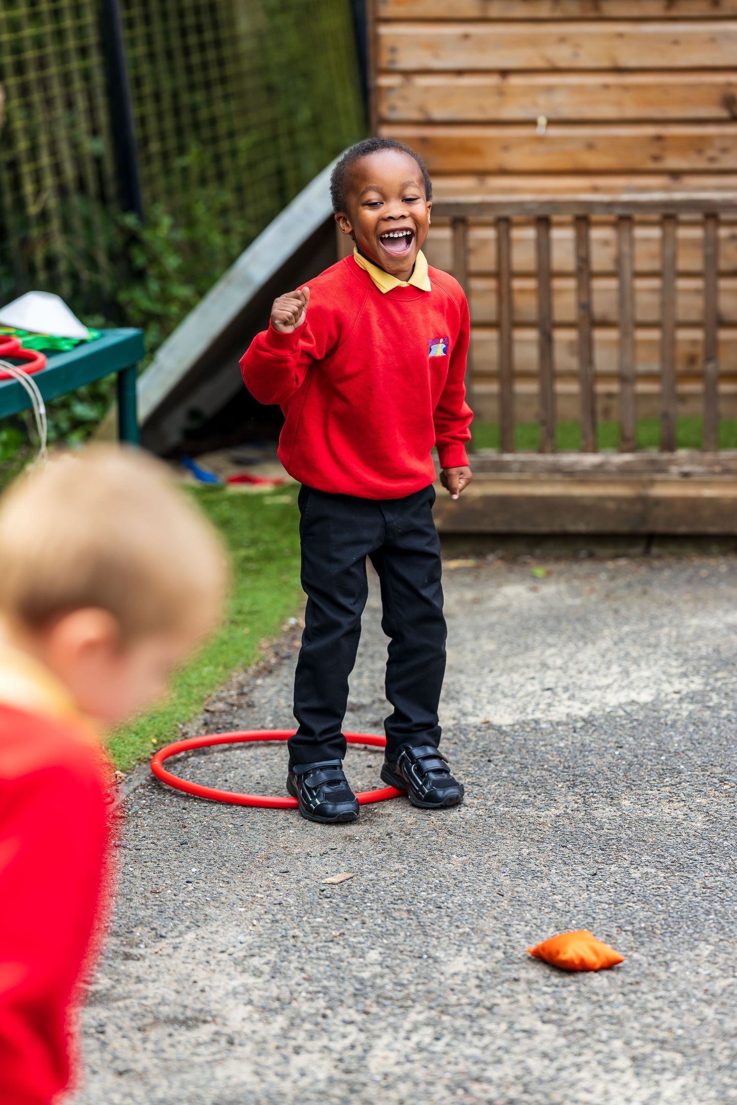 Happy young boy in red school uniform playing with a hula hoop in an outdoor playground in the UK
