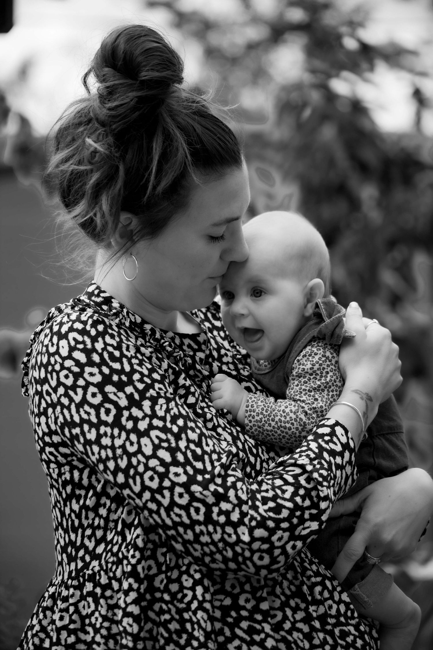 Black and white photo of mother with hair bun in leopard dress holding smiling baby.