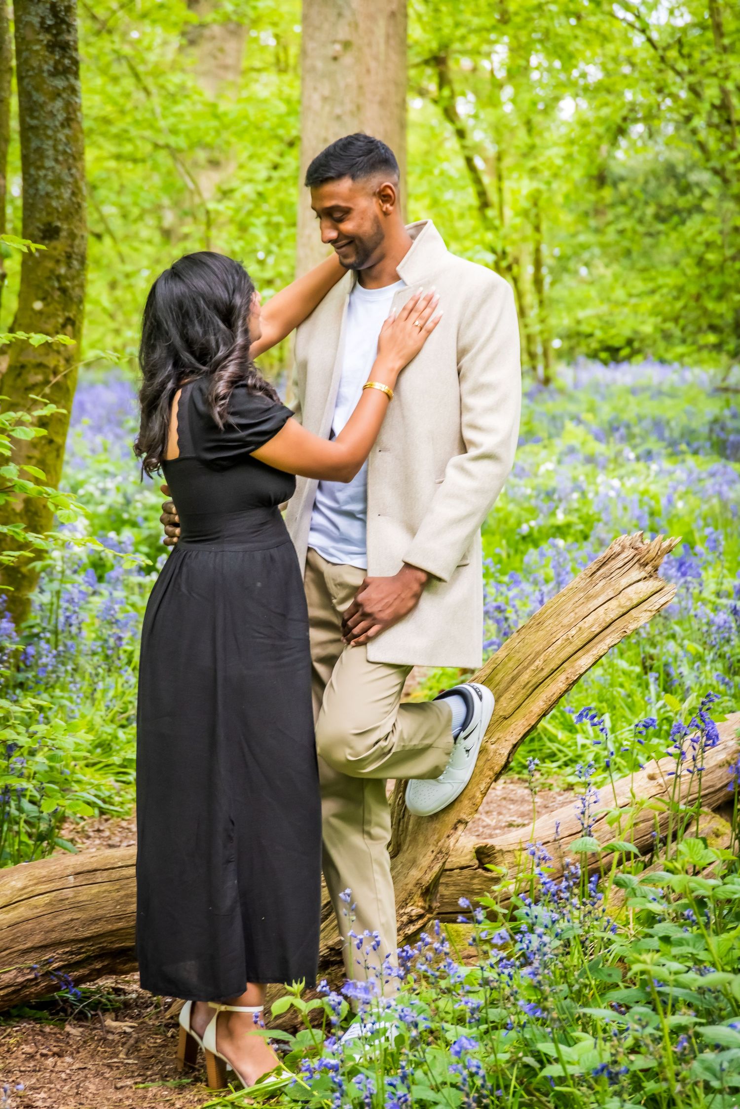 Couple sharing a romantic moment in a bluebell woodland, woman in black dress touches man's face tenderly.