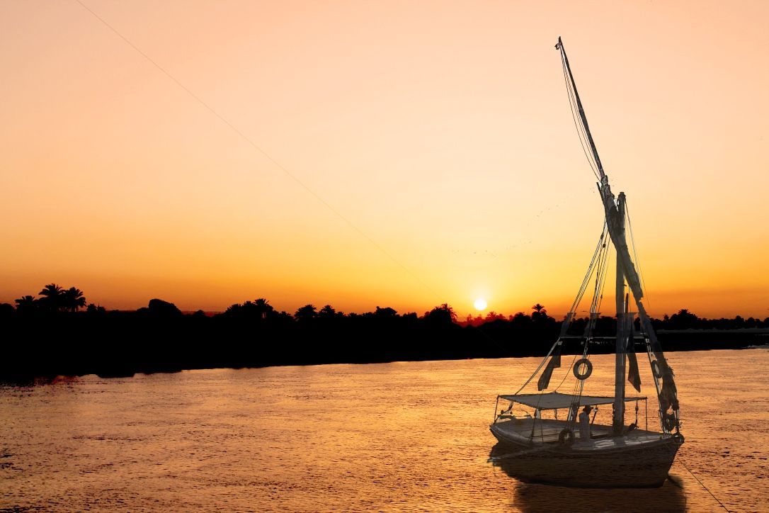Silhouette of a traditional felucca sailboat on the Nile River at golden sunset.