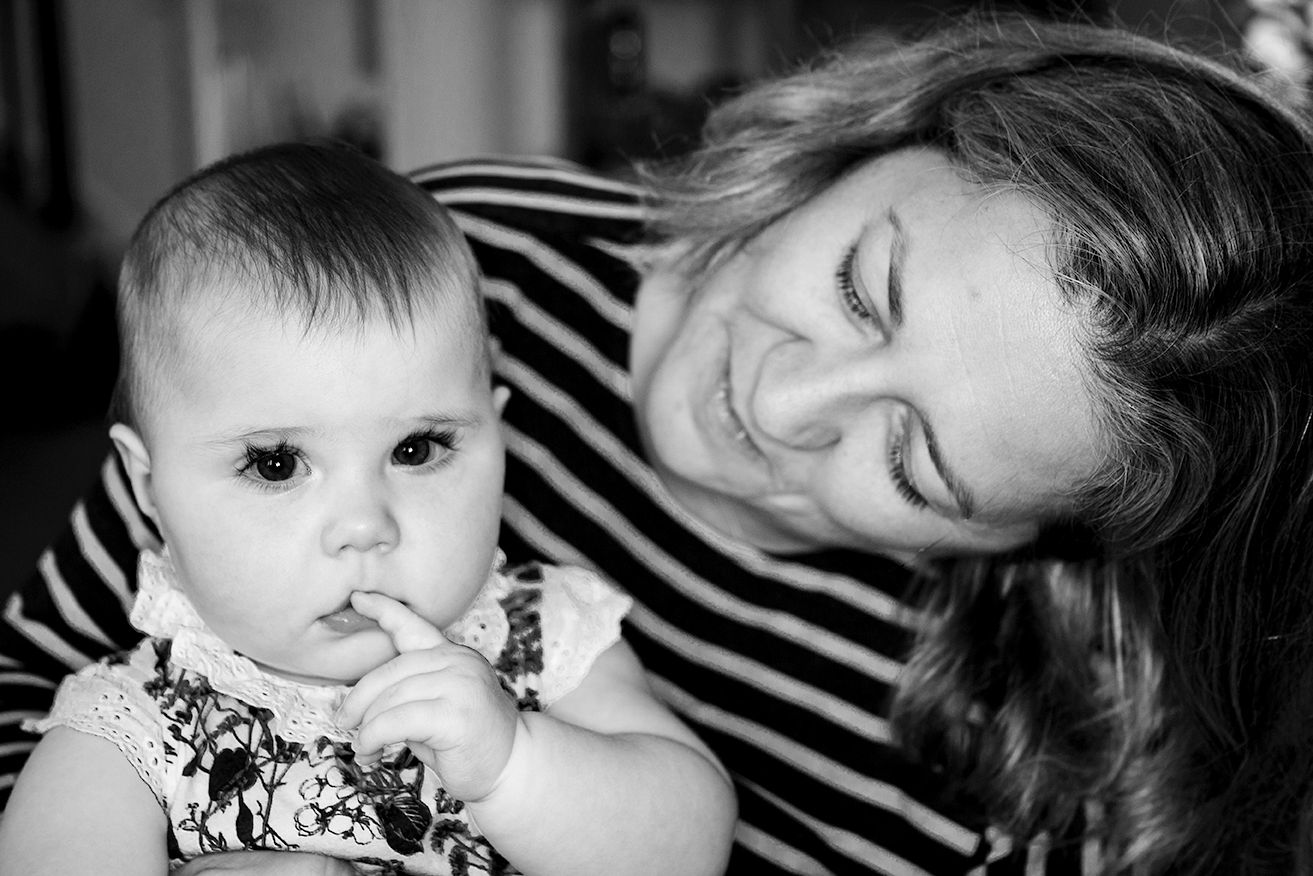 Black and white photo of a mother tenderly looking at her baby girl sucking her finger.