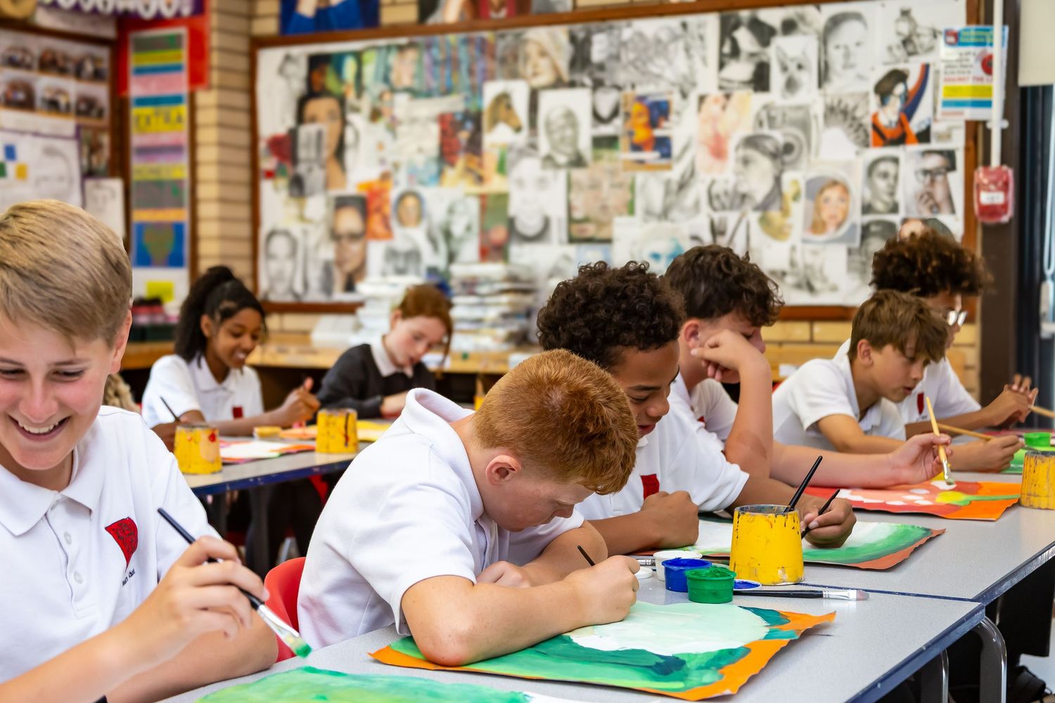 Diverse group of school children drawing and painting at desks in a colorful art classroom.
