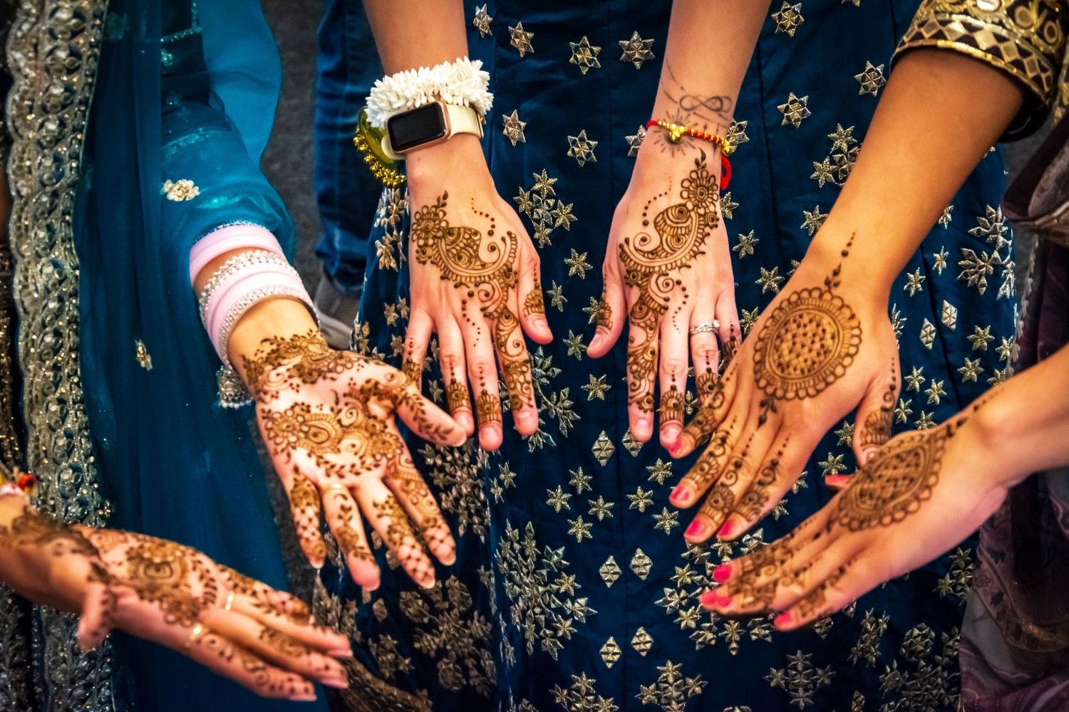 Multiple hands displaying intricate henna mehndi designs at an Indian wedding celebration.