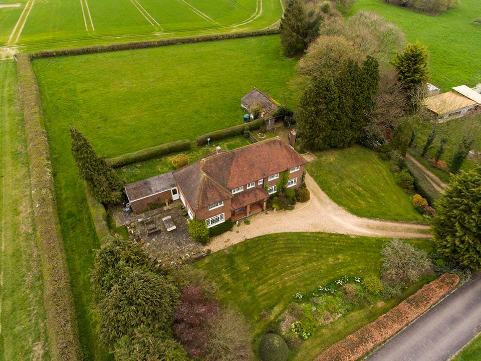 Aerial drone view of a red brick country house surrounded by green fields and trees.