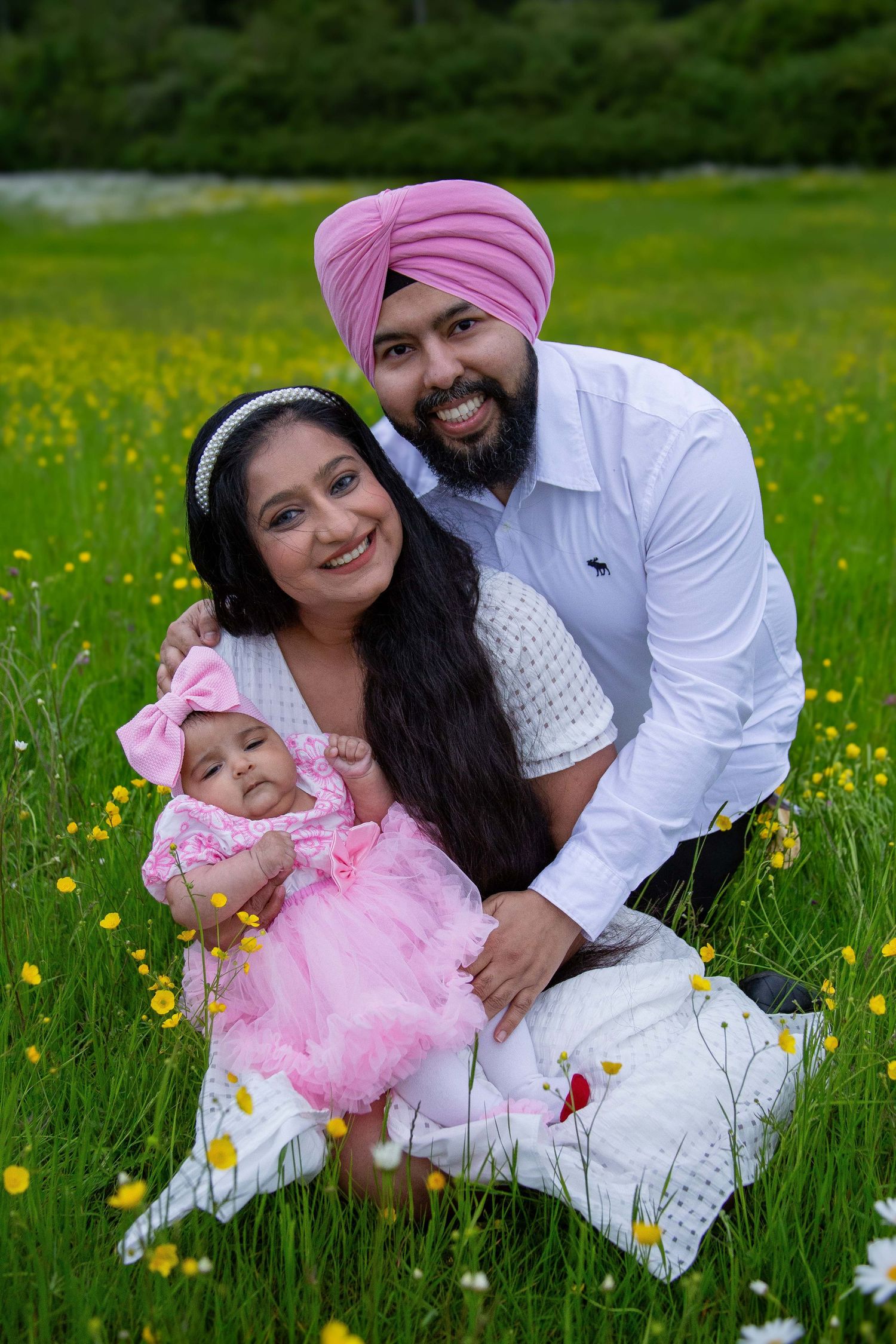 Sikh family portrait in wildflower meadow with father in pink turban, mother, and baby in pink dress.