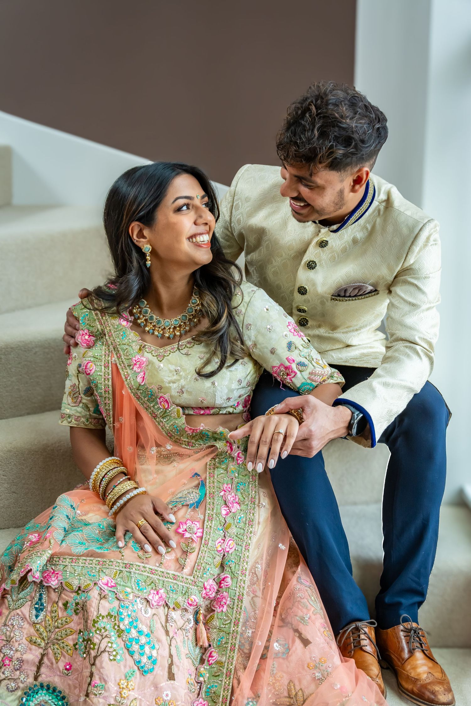 Indian couple in traditional wedding attire sharing a joyful moment on stairs.