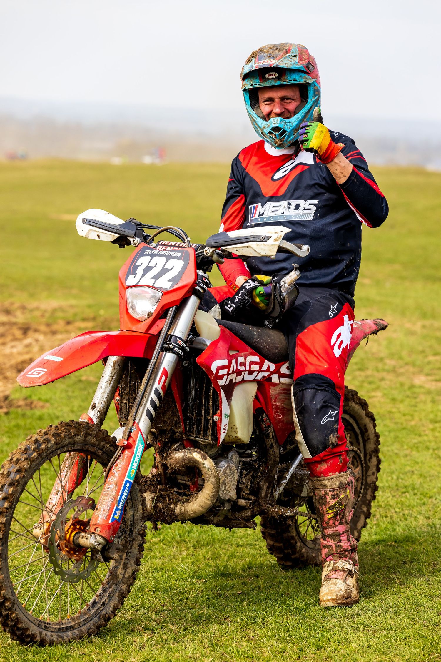 Happy motocross rider in red and blue gear on a dirt bike. Event photography taken by Roddy Lloyd-Jones
