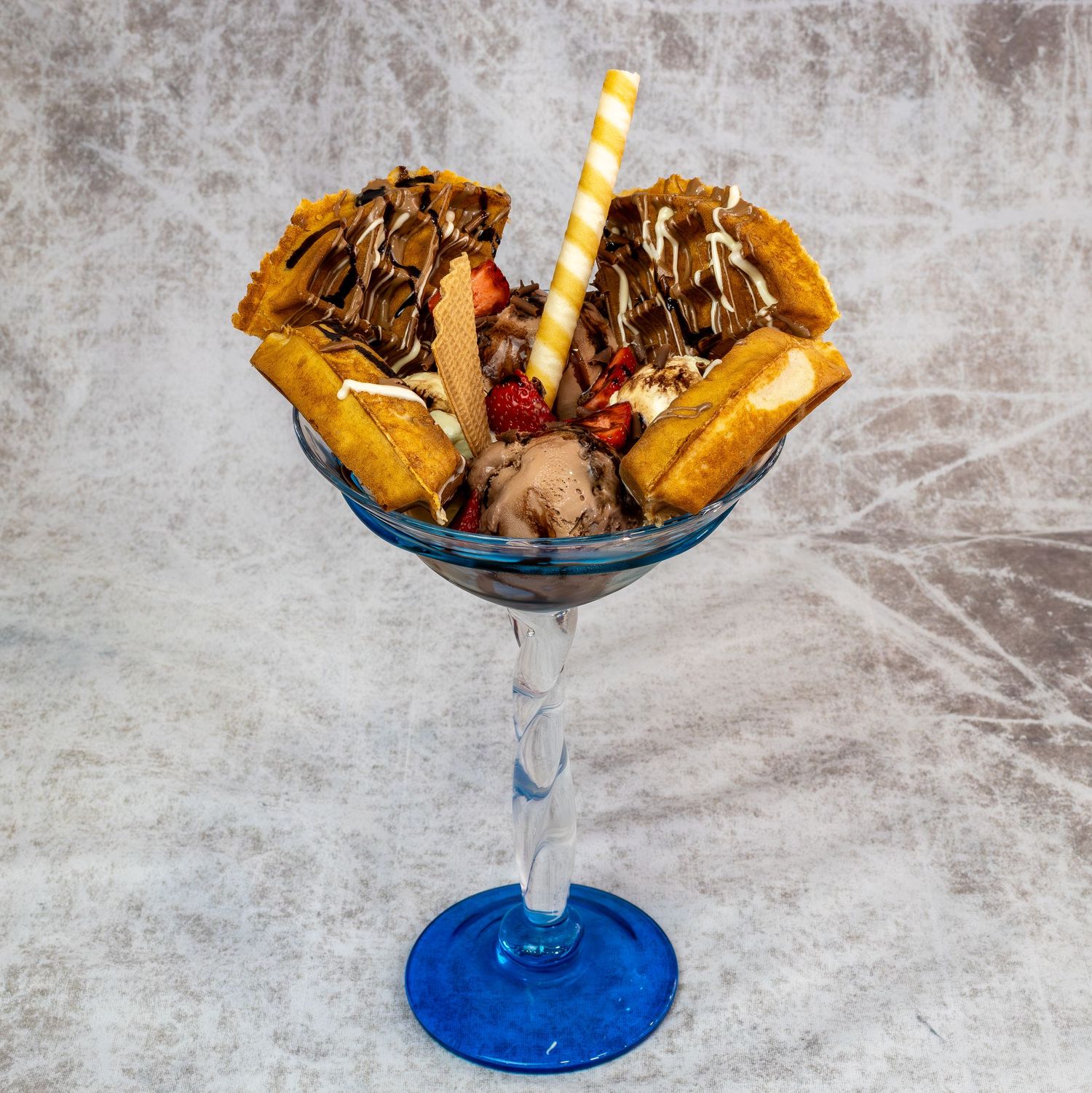 Decadent ice cream sundae with waffles and chocolate drizzle in a blue martini glass. Product shoot for menu.