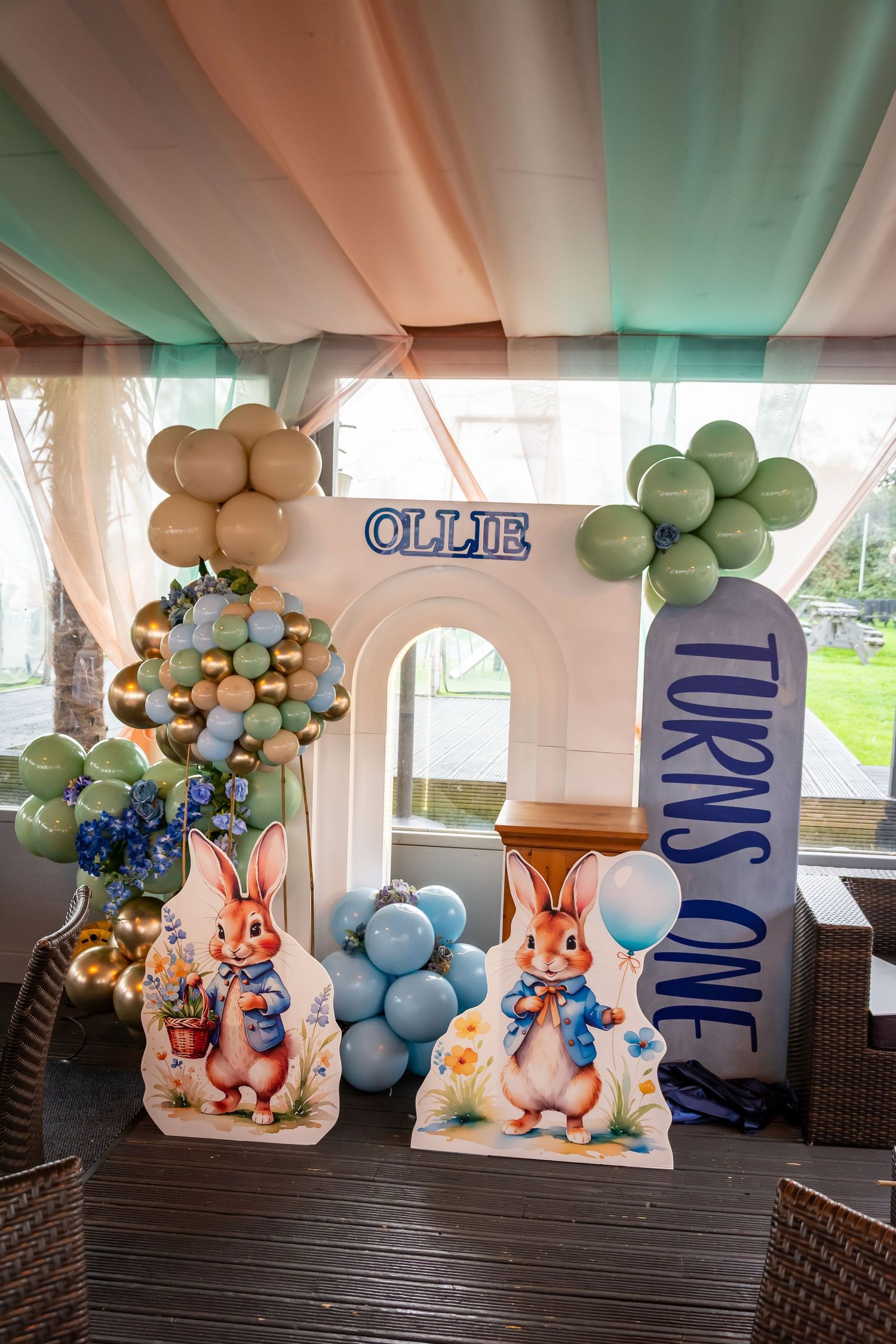Peter Rabbit themed first birthday party decoration with balloons and cutouts reading Ollie Turns One.