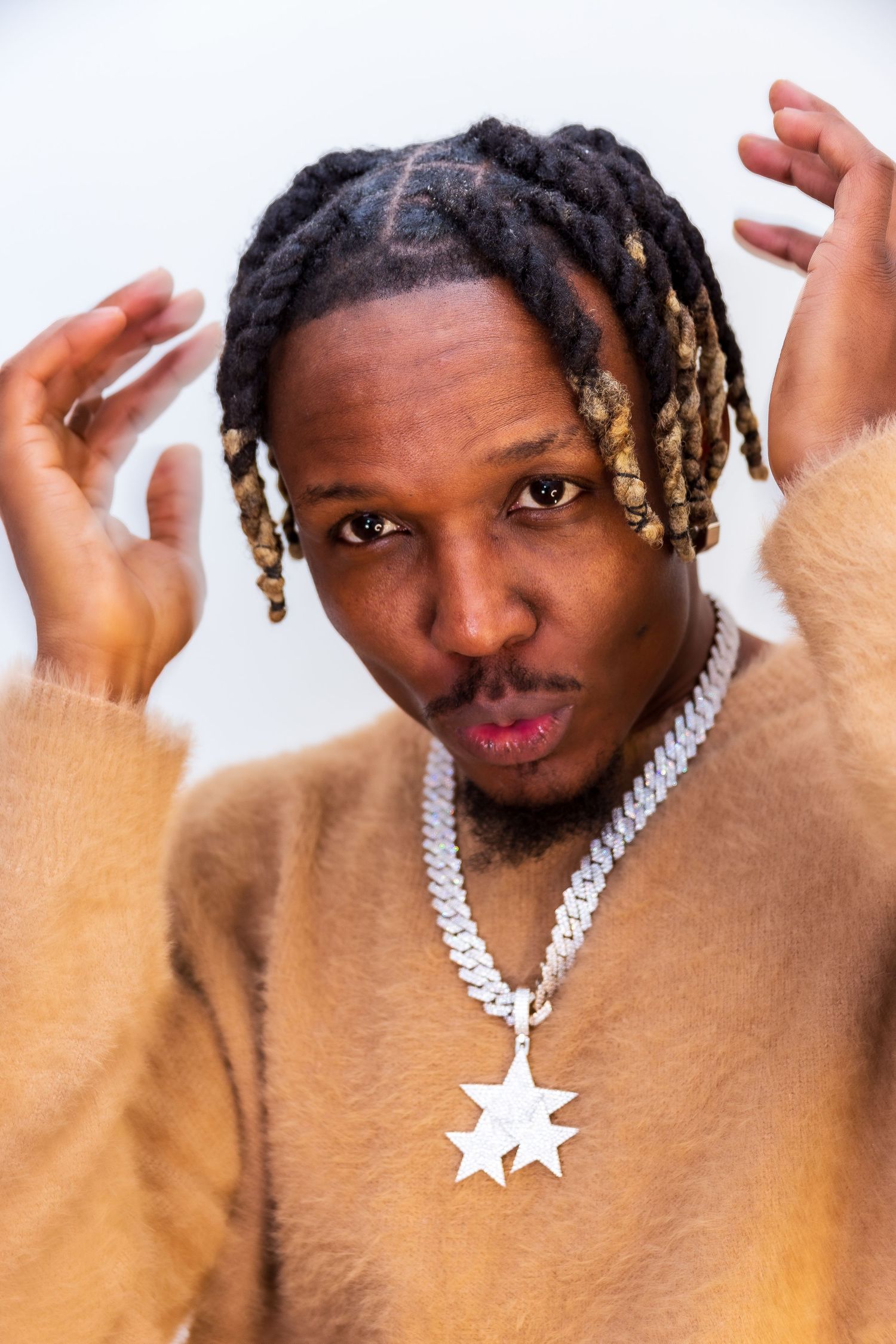 Man with dreadlocks wearing a beige fuzzy sweater and star pendant chain necklace posing indoors. Modelling photoshoot.