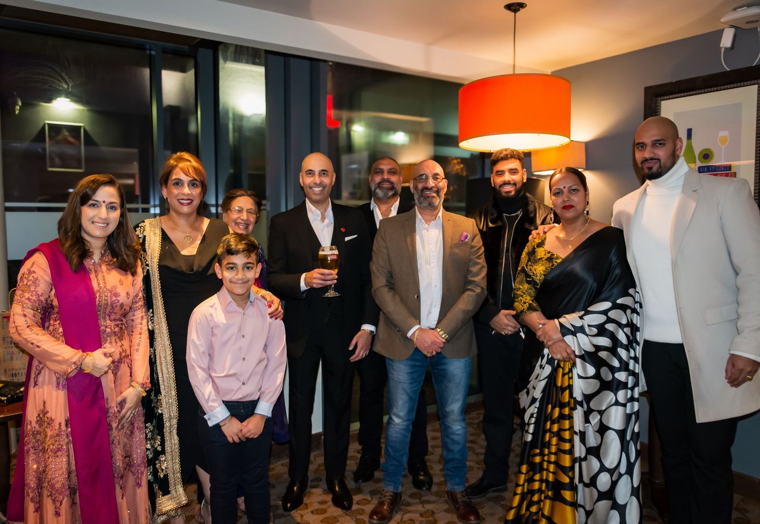 Group of South Asian family and friends posing together at an indoor celebration event.