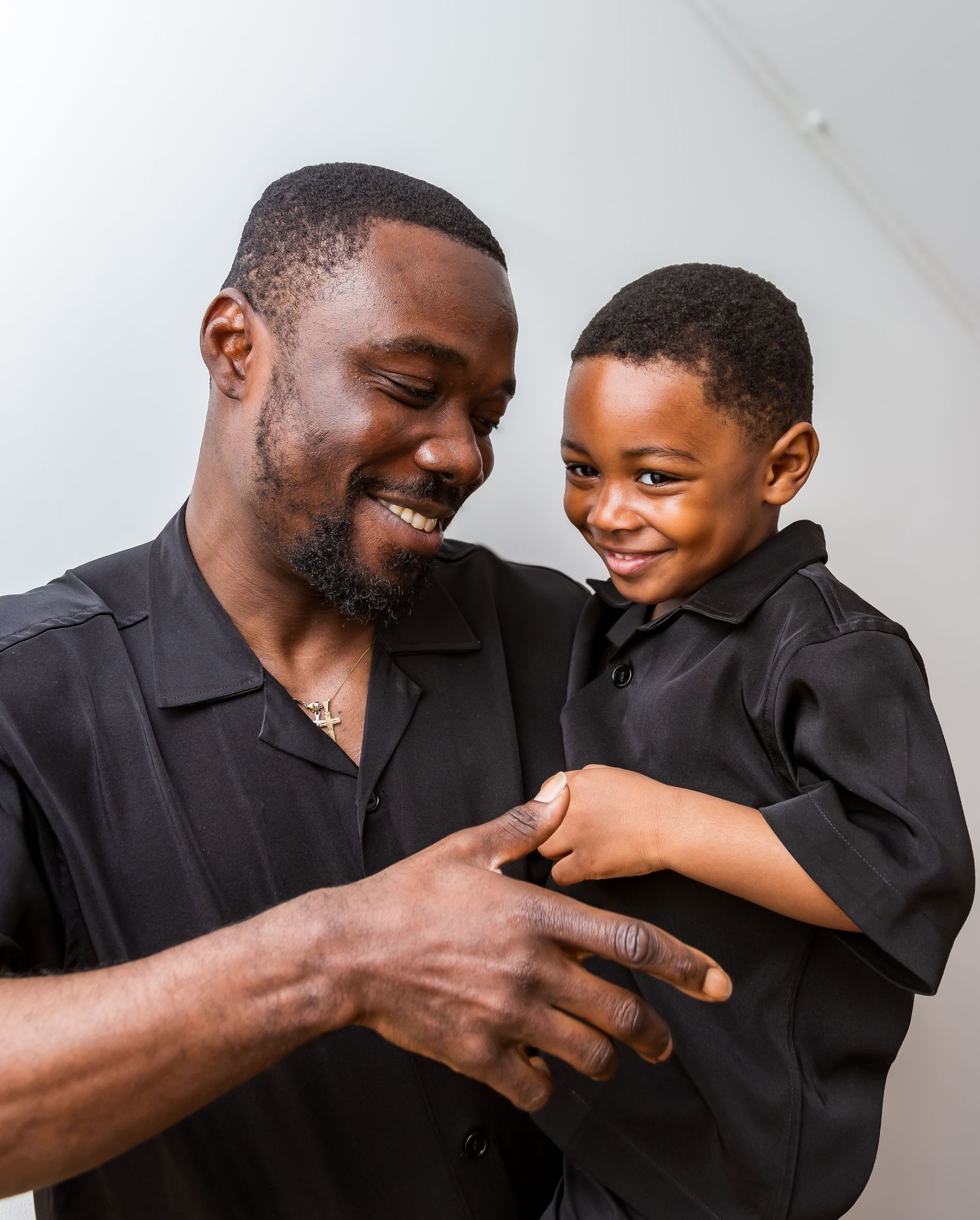 Smiling man in black shirt holding young boy in matching outfit during a portrait session.