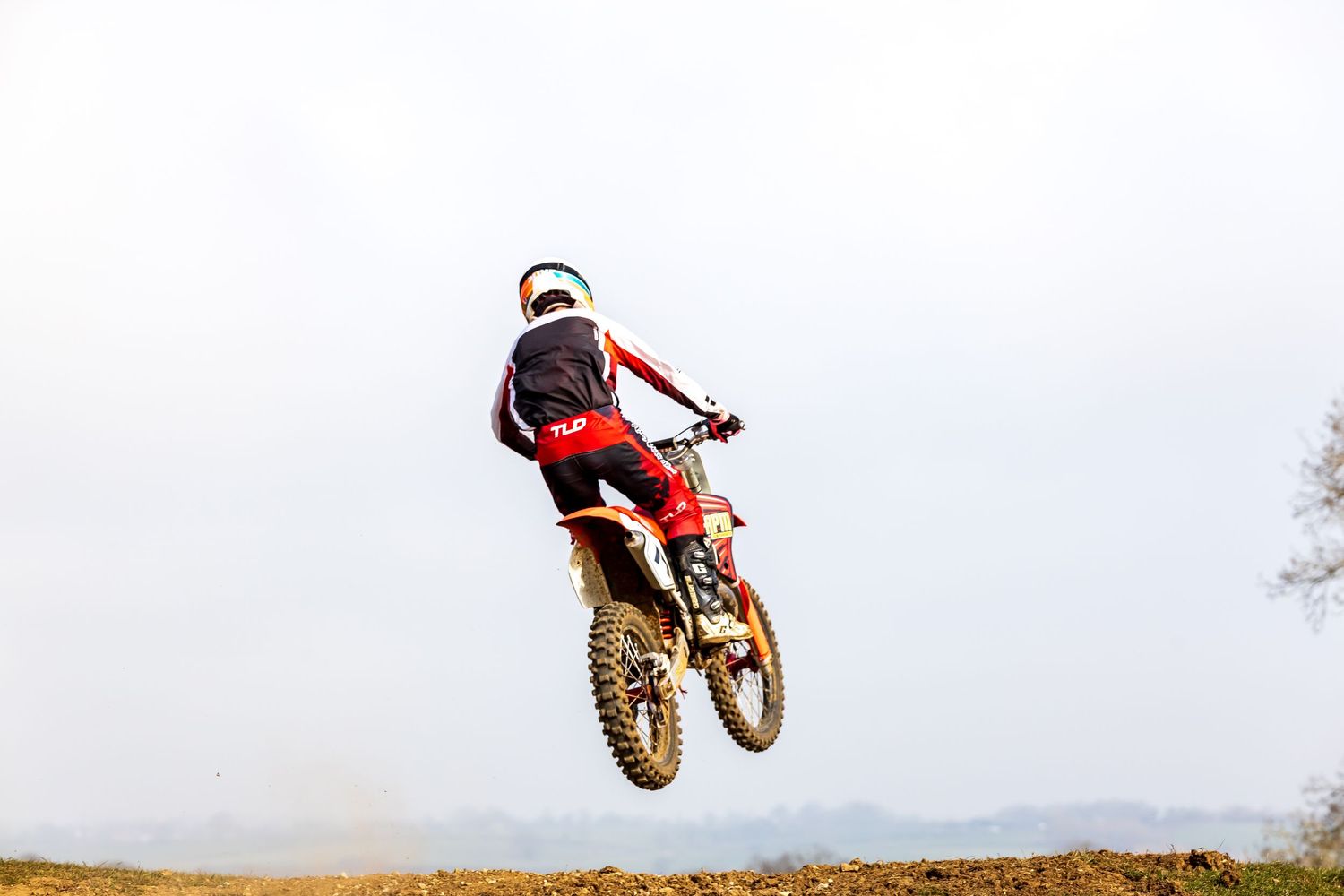Motocross rider performing a high jump on a red dirt bike against a cloudy sky backdrop. Shot by LJPhotostop.