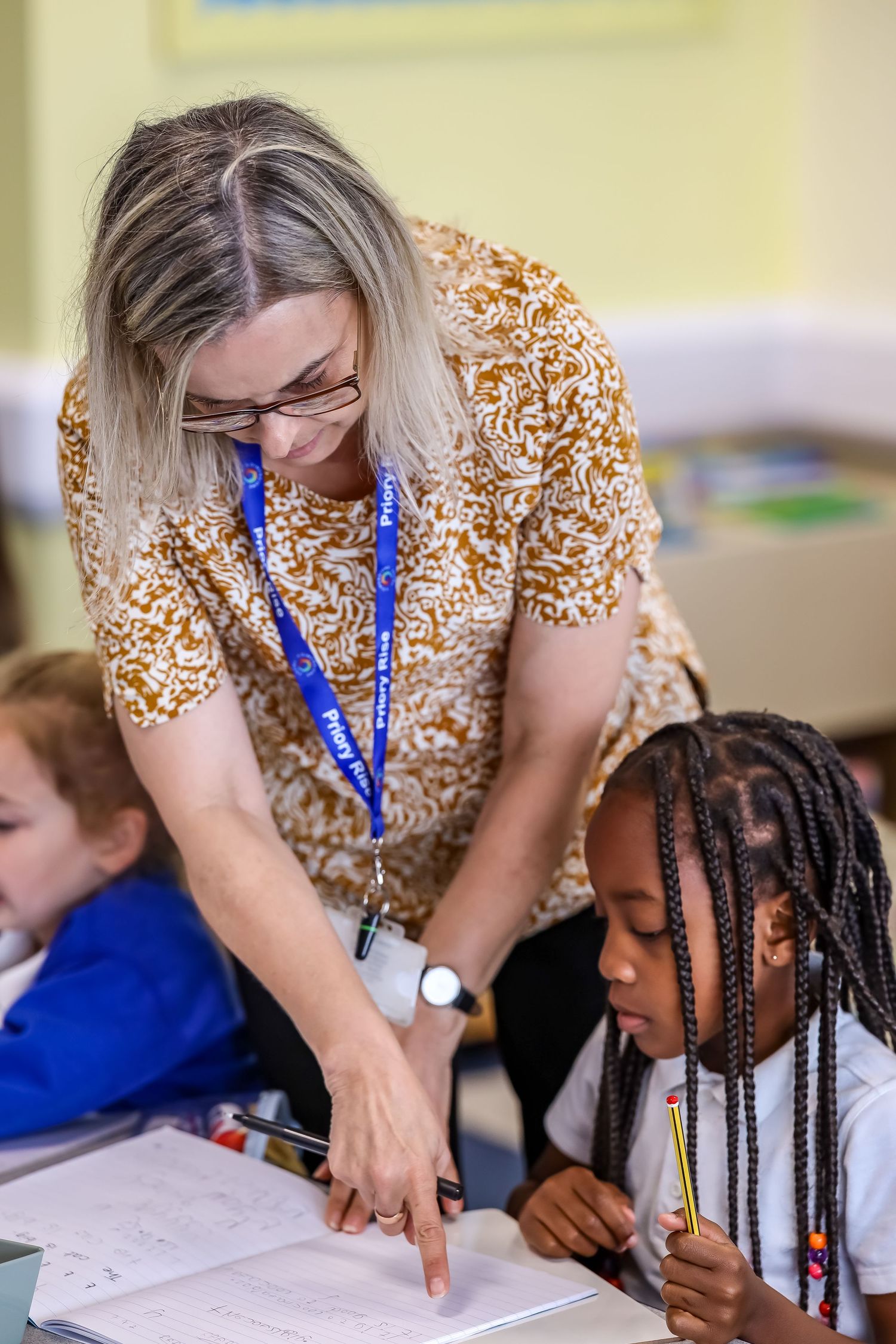 Teacher pointing at a notebook helping a young girl during class.