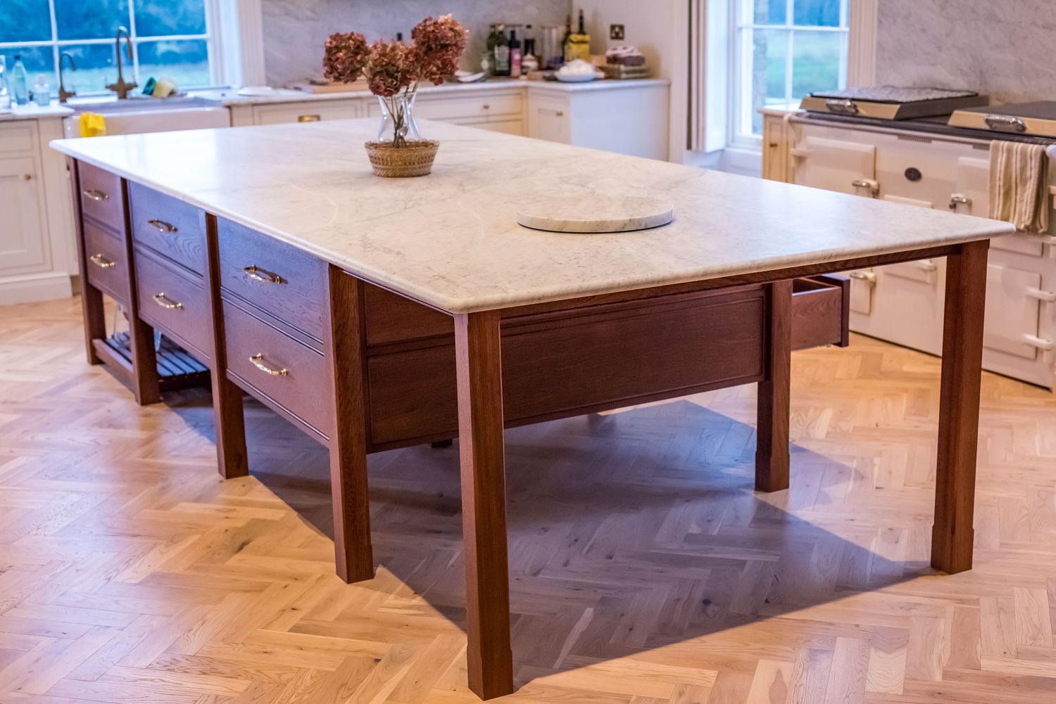 A large kitchen island with a white marble countertop and dark wood base on herringbone parquet flooring.