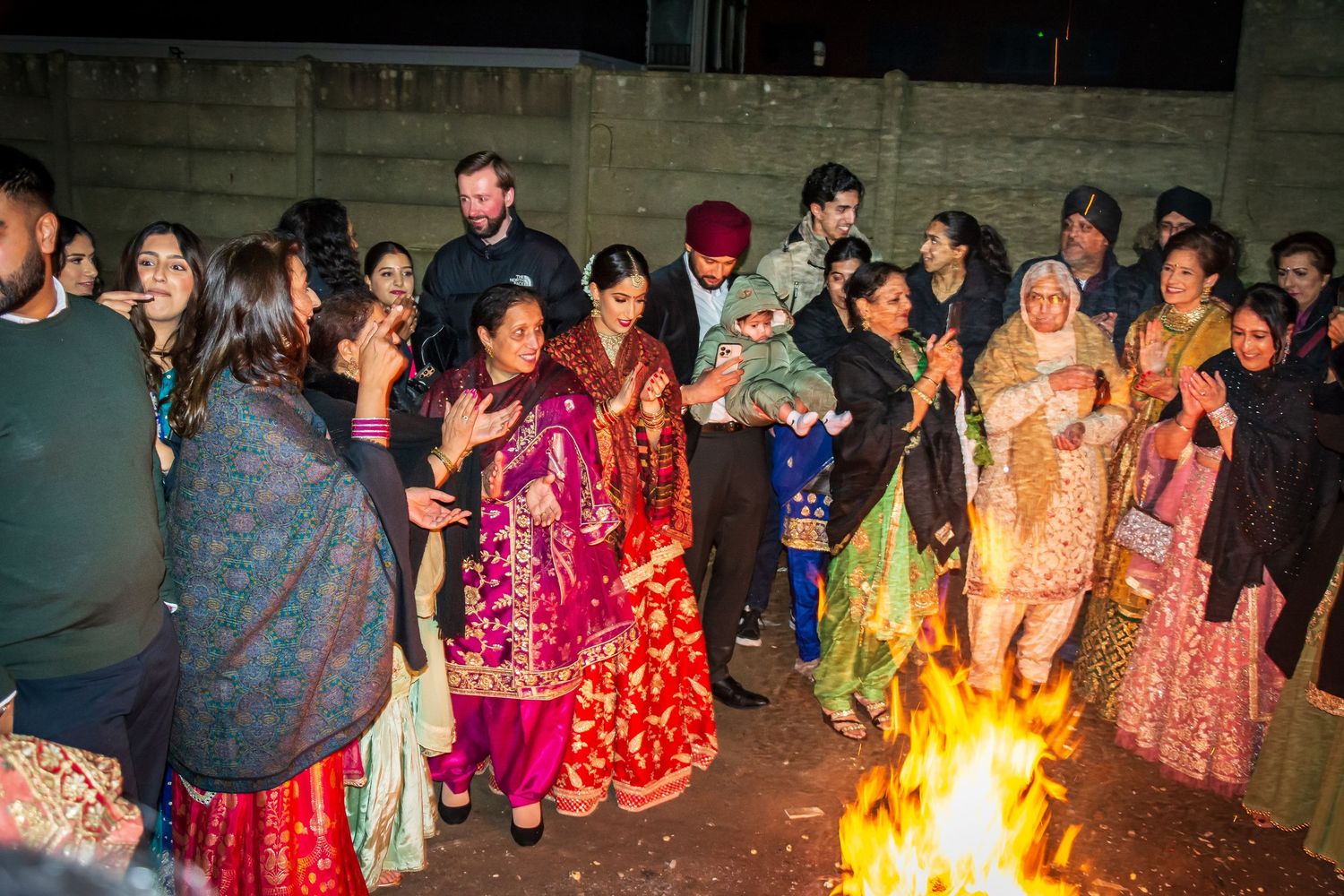 Group of people in colorful traditional Indian clothing dancing around a bonfire at Lohri.