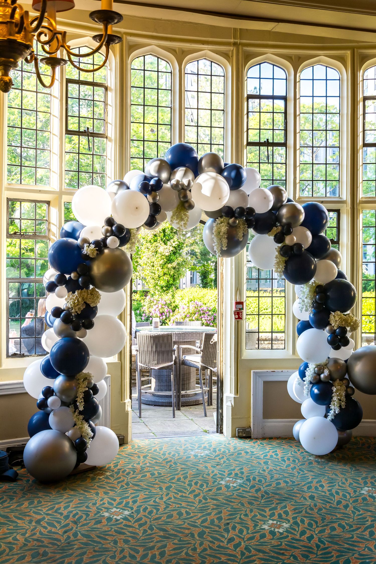Elegant balloon arch in navy, white, and silver decorating a grand venue doorway.