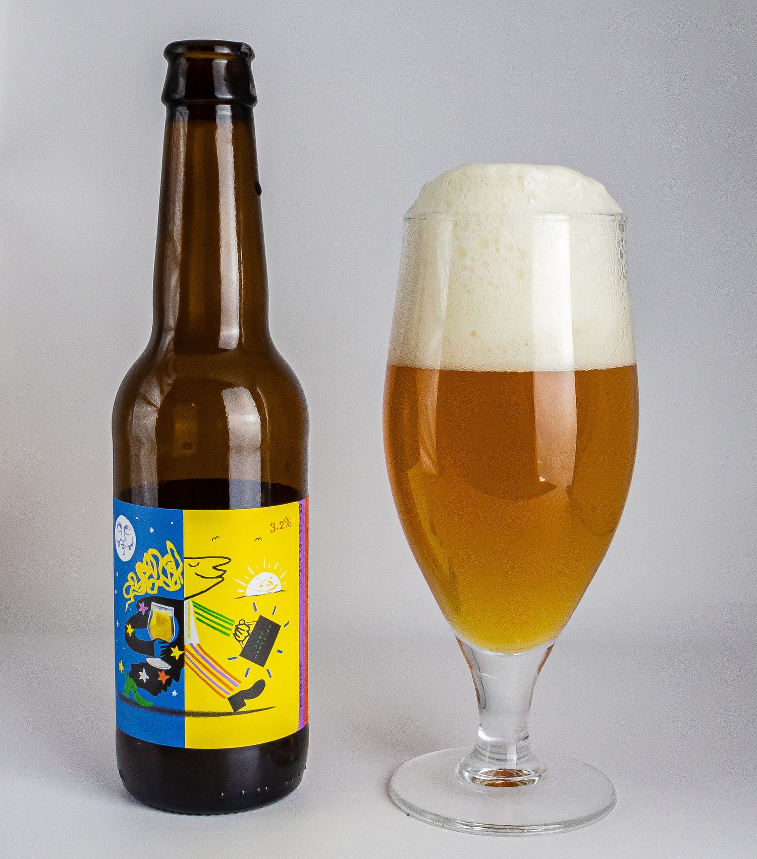 Craft beer bottle with colorful label beside full frothy glass on light gray background.