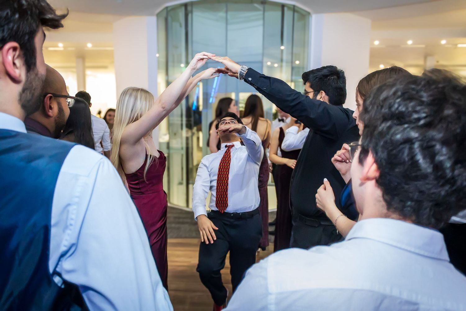 Group of young adults dancing in a circle at a lively party celebration indoors.