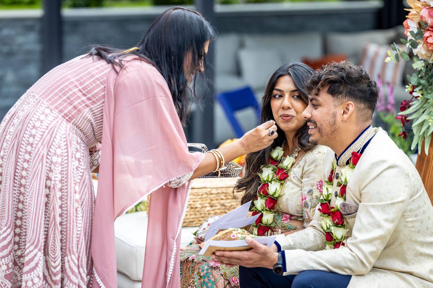 Elder woman performing a traditional Indian wedding ritual blessing the couple with sweets.