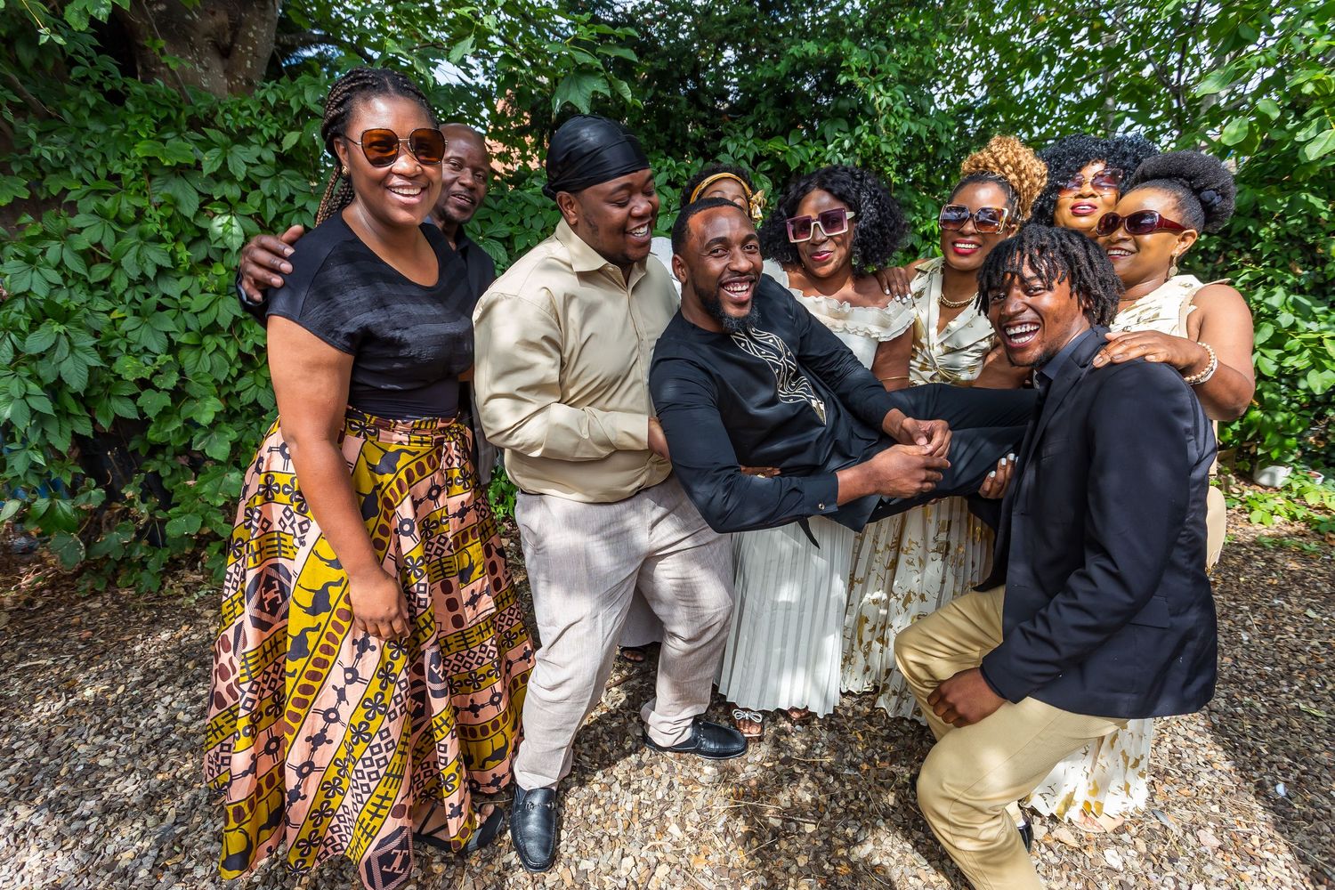 Group of eight wedding guests smiling and posing together under green foliage.