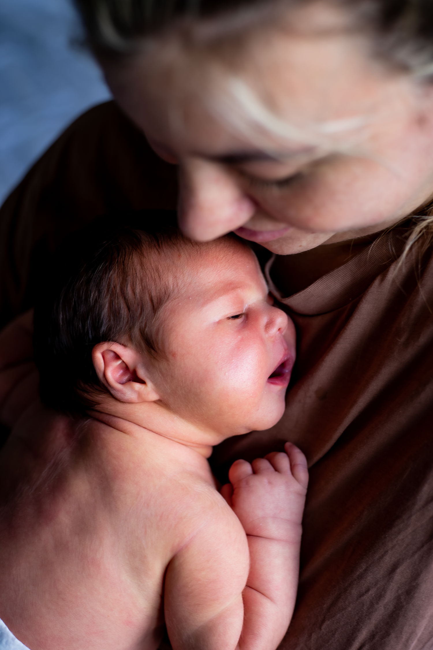 A tender moment as a mother gently kisses her sleeping newborn baby held close to her chest.