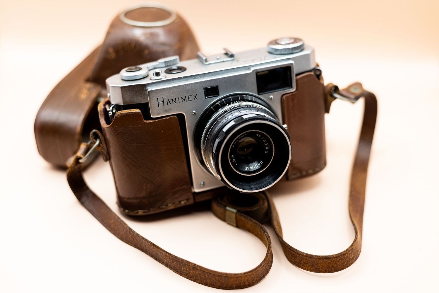 Vintage Halina 35mm film camera in brown leather case with strap on beige background.