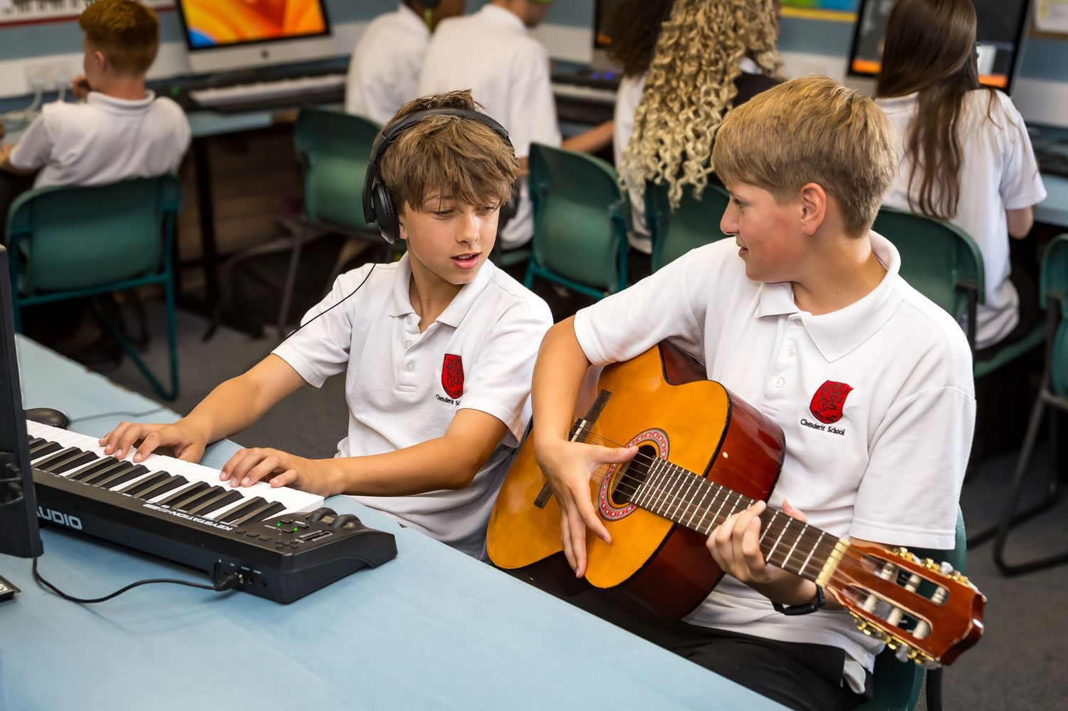 Two school boys playing keyboard and guitar together during a music lesson in class.