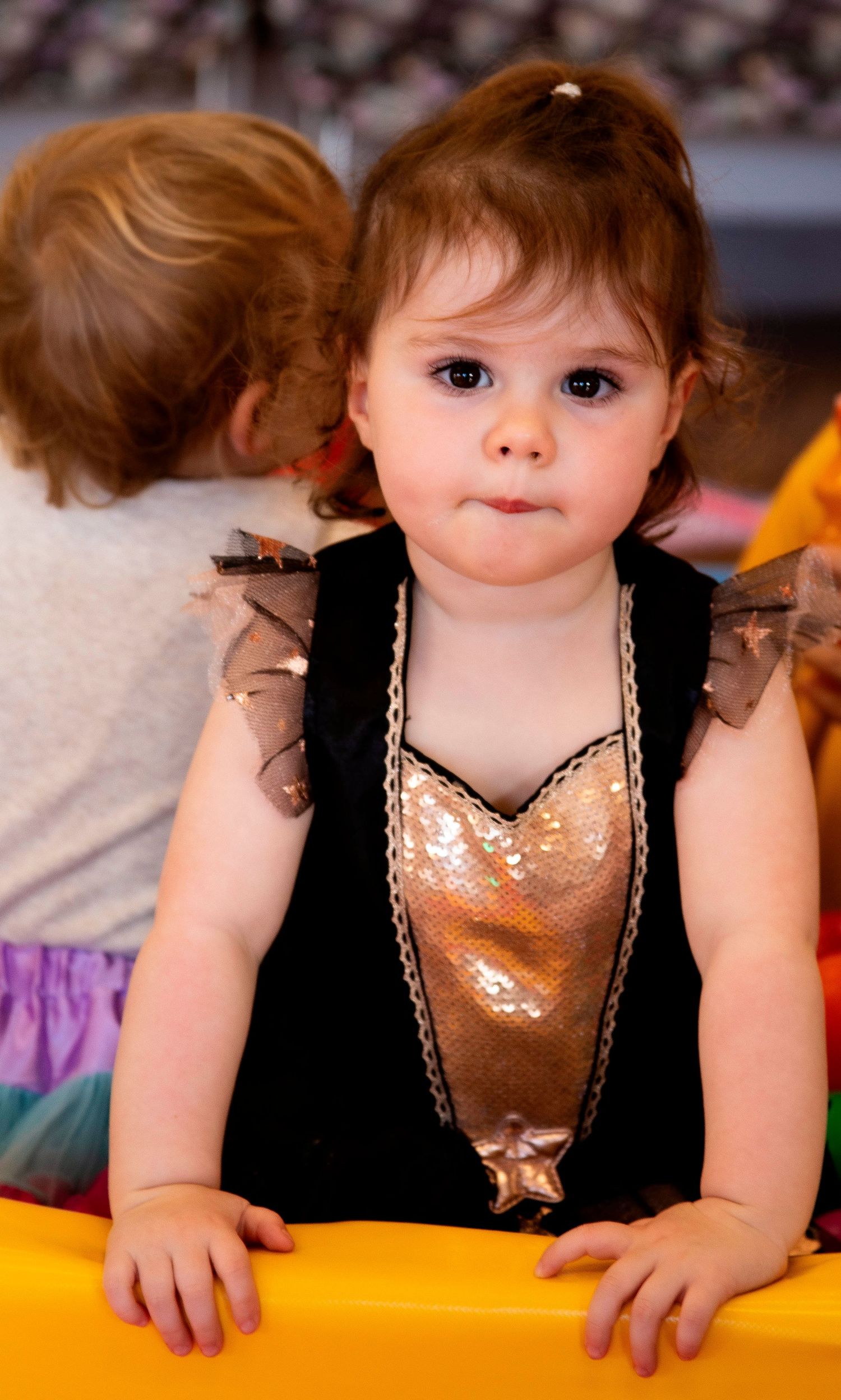 An adorable toddler girl in a black sequin dress with tulle sleeves at a children's party.