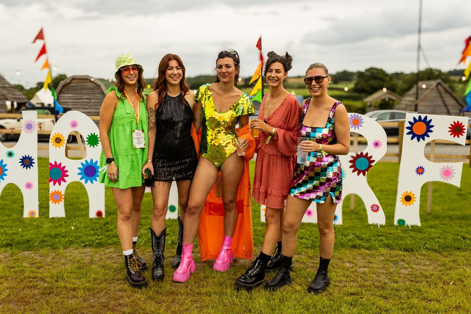 Five women in colorful festival outfits posing together in front of decorative festival signage.