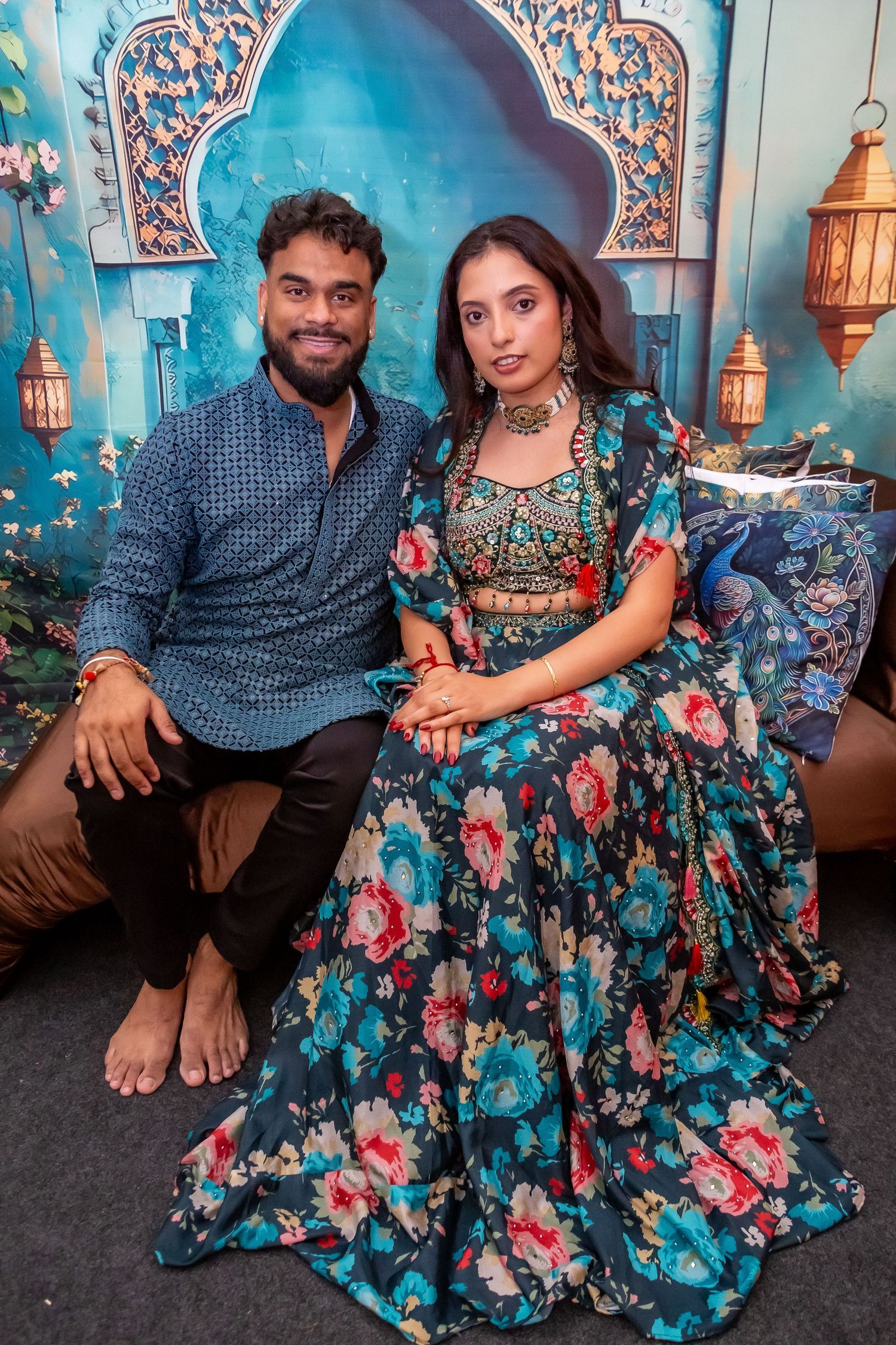 Indian couple posing together at a celebration, woman wearing a floral teal lehenga and man in blue kurta.