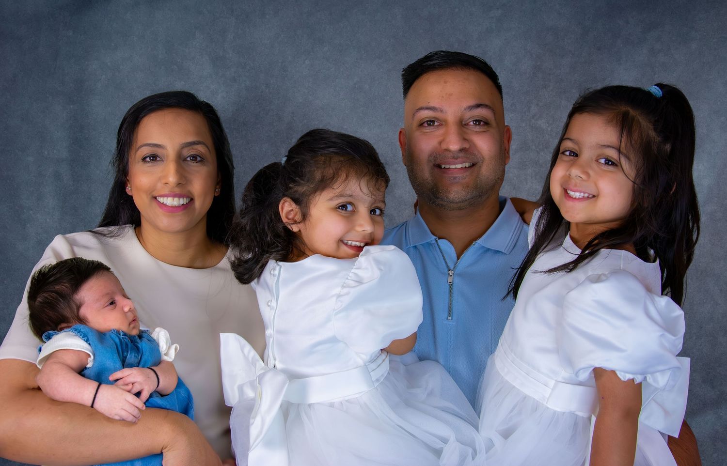 Family studio portrait with parents, two daughters in white dresses, and newborn baby boy.