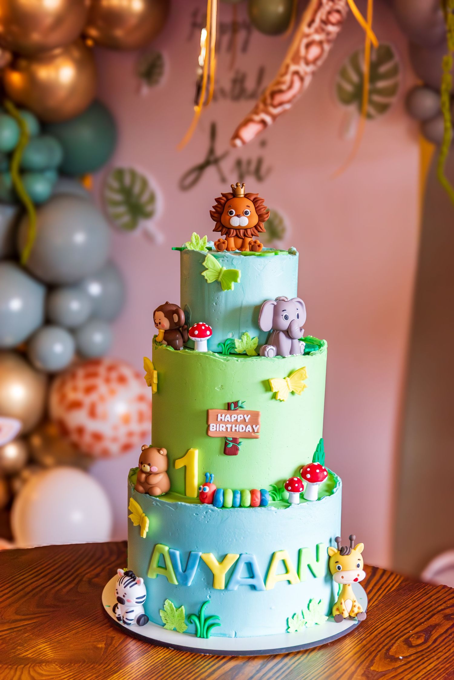 A three-tier jungle safari themed birthday cake decorated with animal figurines for Avyaan's 1st birthday.
