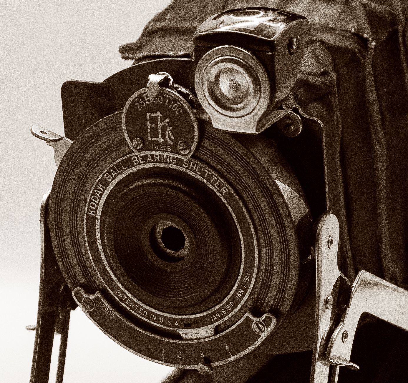 Close-up sepia tone of antique Kodak Ball Bearing Shutter folding camera lens detail.