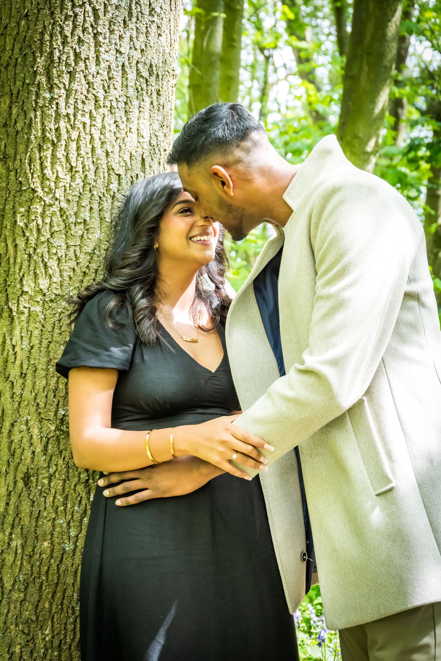 Couple sharing a romantic moment leaning against a tree in a lush green woodland.