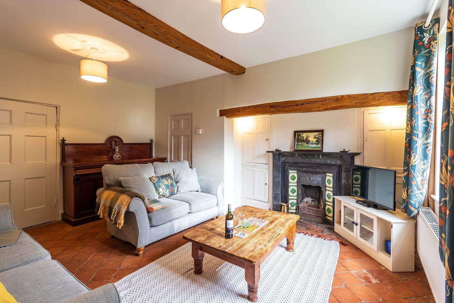 Rustic cottage living room with exposed beams, fireplace, and comfortable sofas.