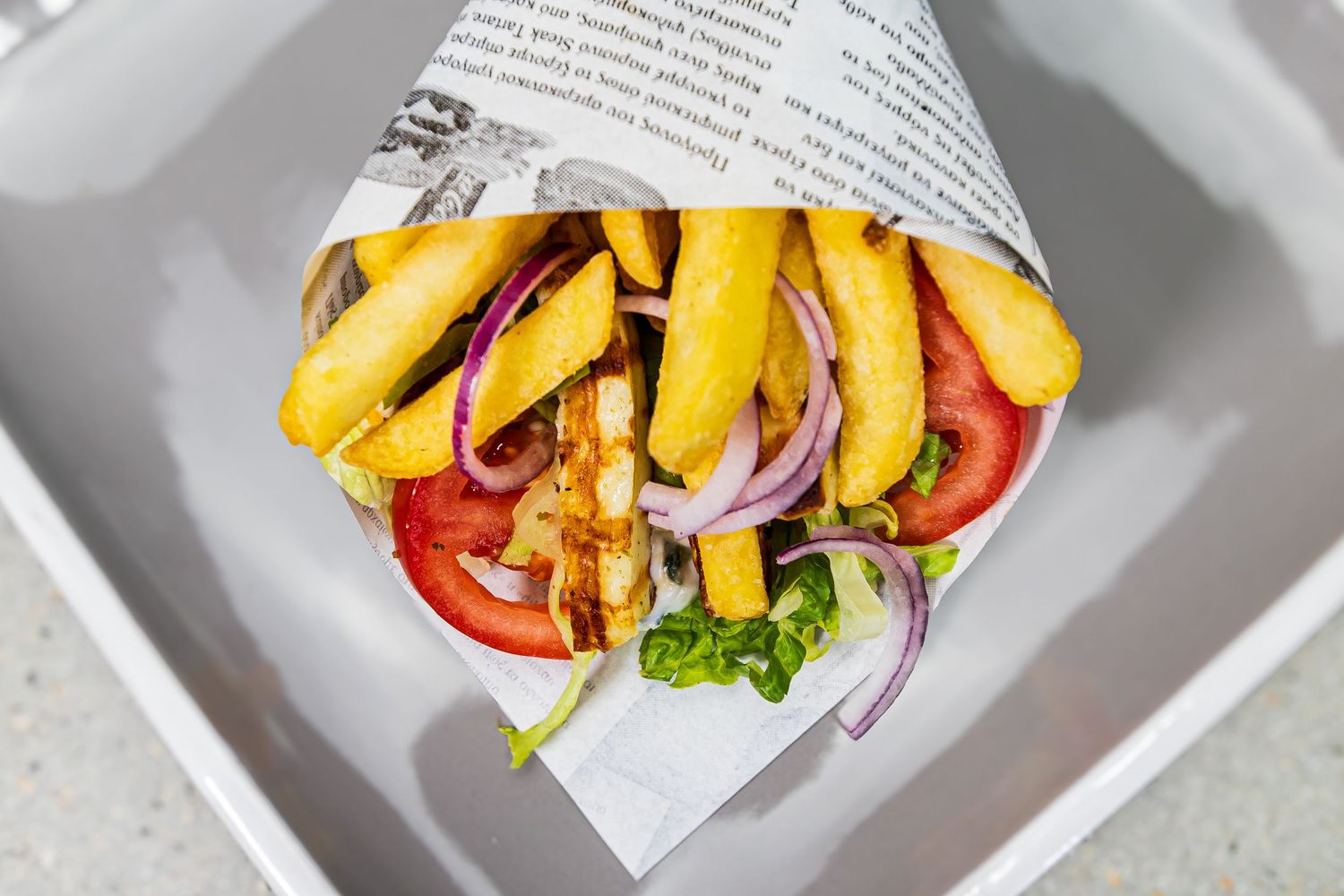 Greek gyro wrap with fries, tomatoes, red onions, and chicken served in paper cone.