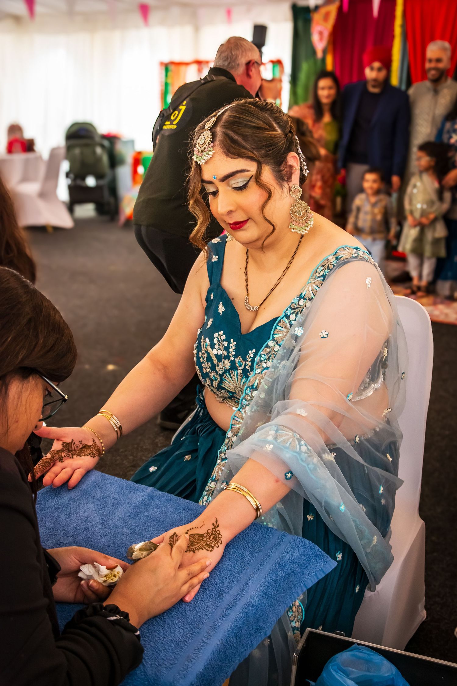 Bride in teal saree having intricate henna mehndi applied to her hands at a wedding ceremony.