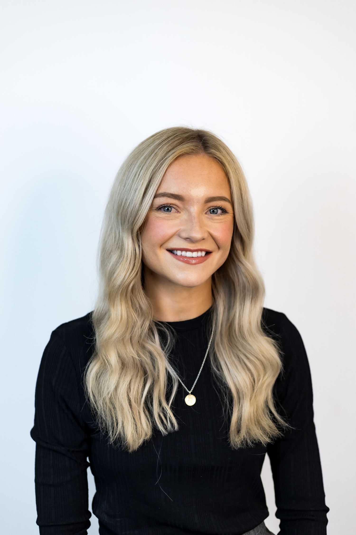 Smiling young blonde woman wearing black top and gold necklace in professional headshot photo.