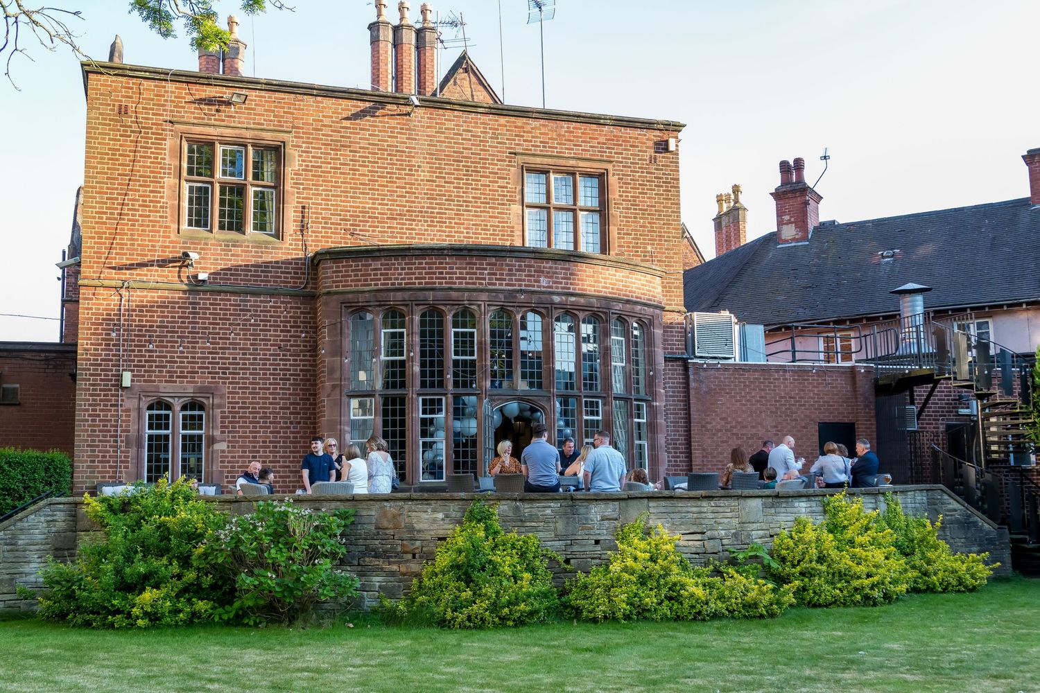 Guests socializing outdoors at a brick building venue during a summer evening event.