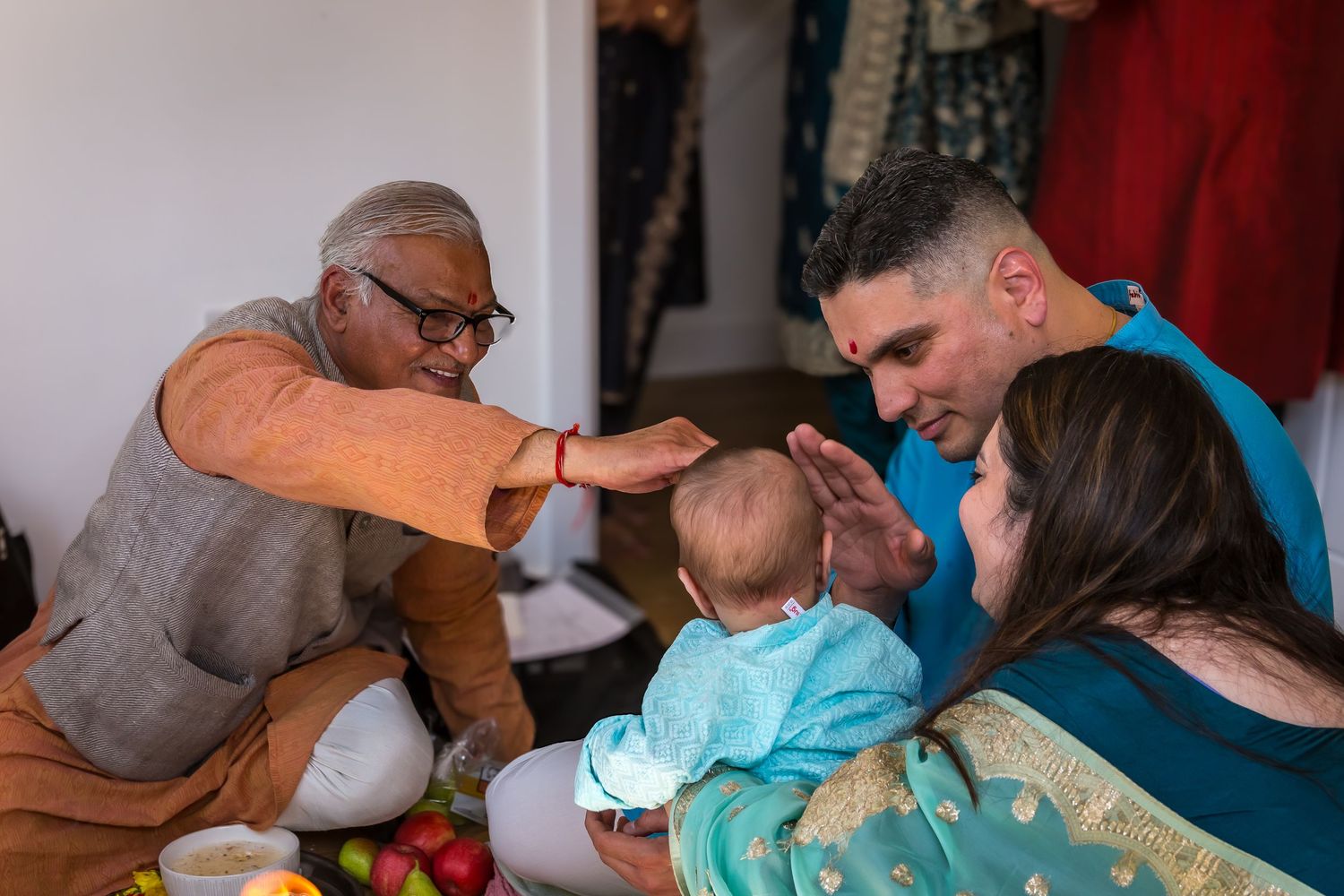 Hindu priest performs baby naming ceremony blessing infant held by parents during traditional ritual.
