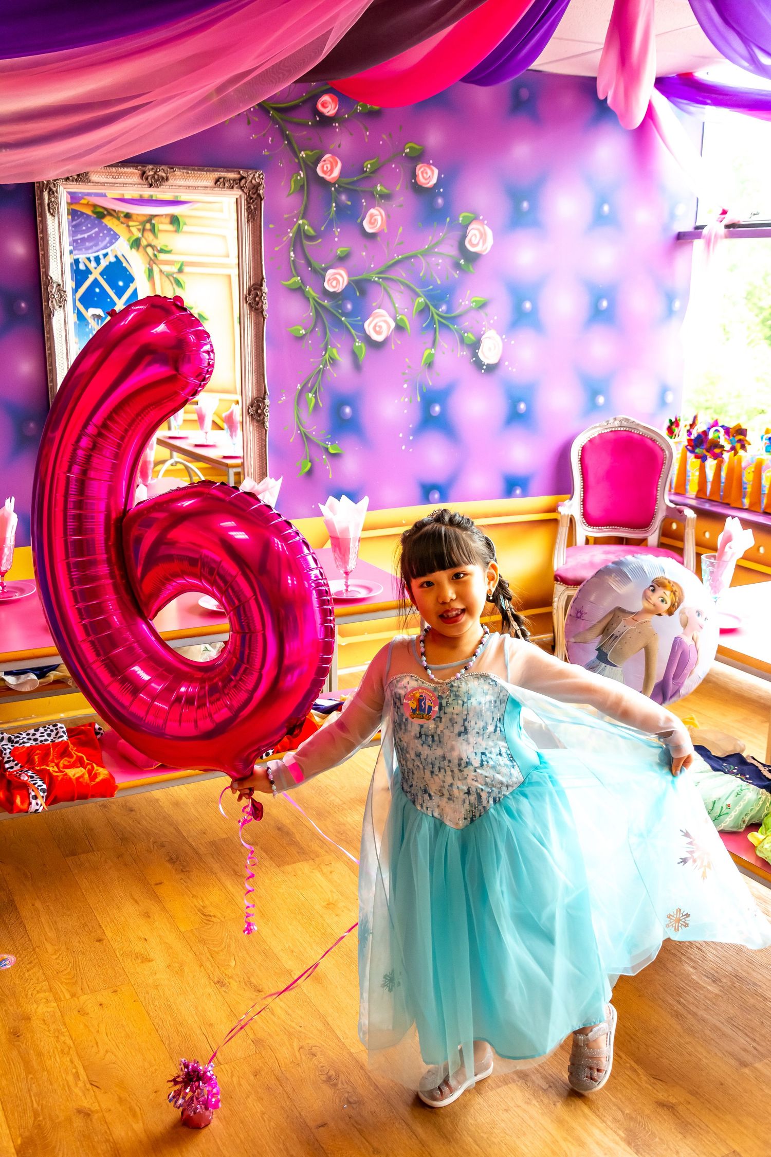 Young girl in Elsa costume celebrating her 6th birthday in a purple princess-themed party room.