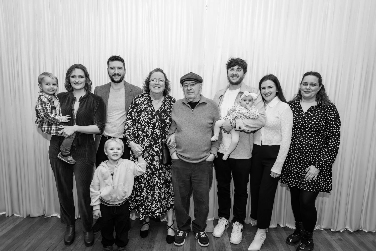 Black and white family group photo of nine people smiling together indoors.