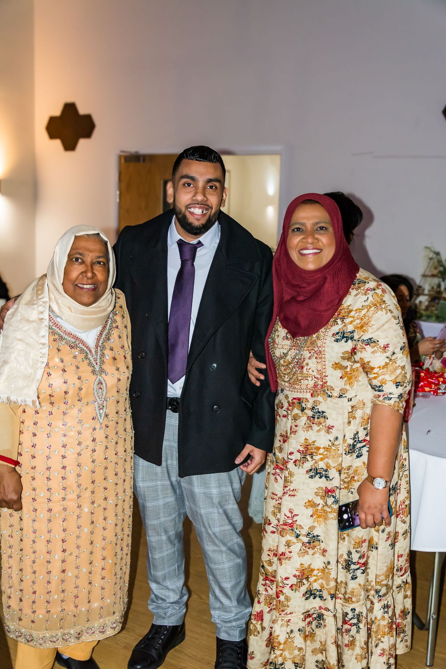 Young man smiling with two older women in traditional dress at a family celebration event.