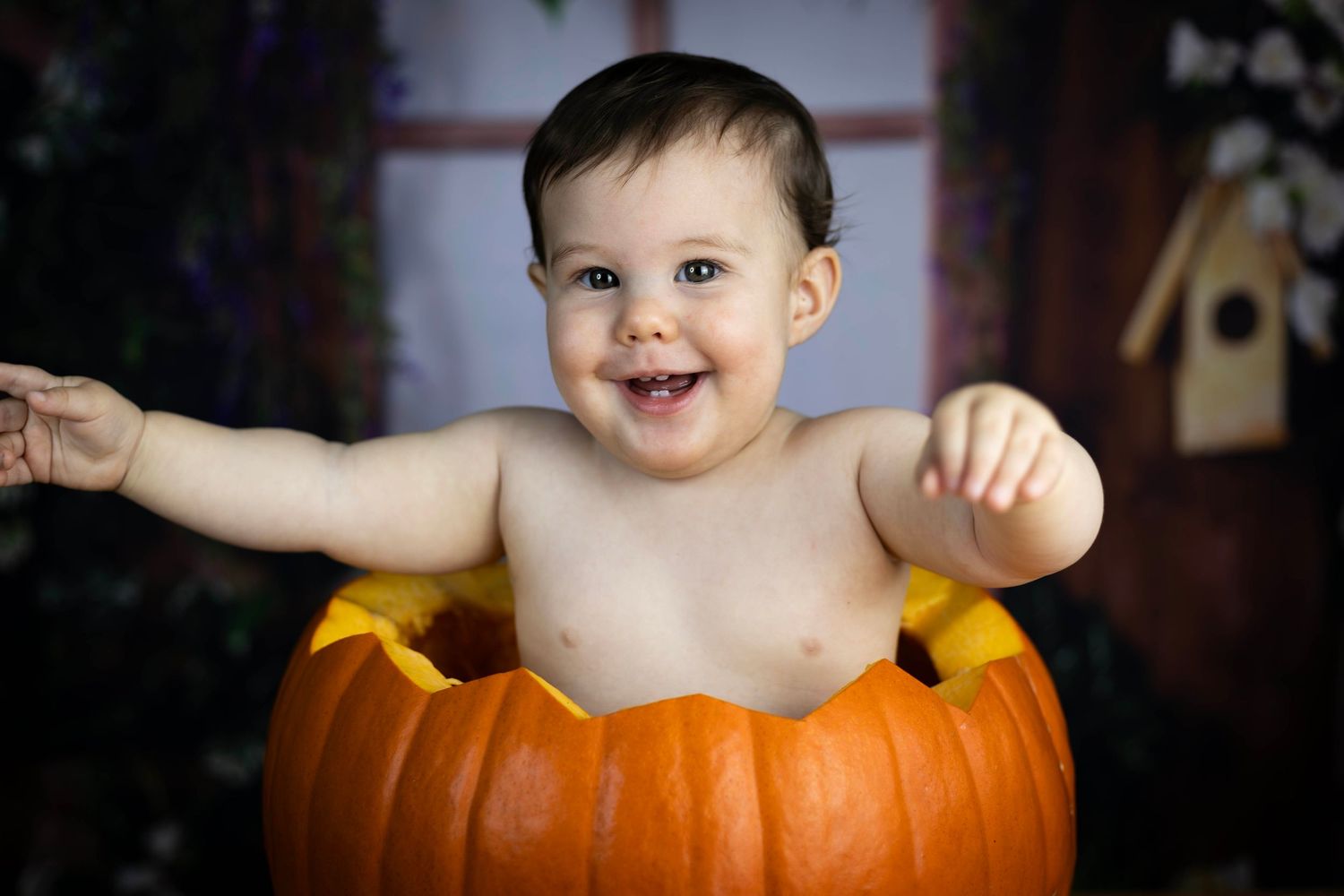 Happy smiling baby sitting inside a large carved Halloween pumpkin with arms outstretched.
